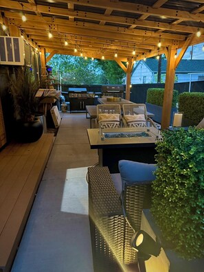 An outdoor patio area with a grill, seating, and string lights. - Central R&R Cape Cod (Casper)