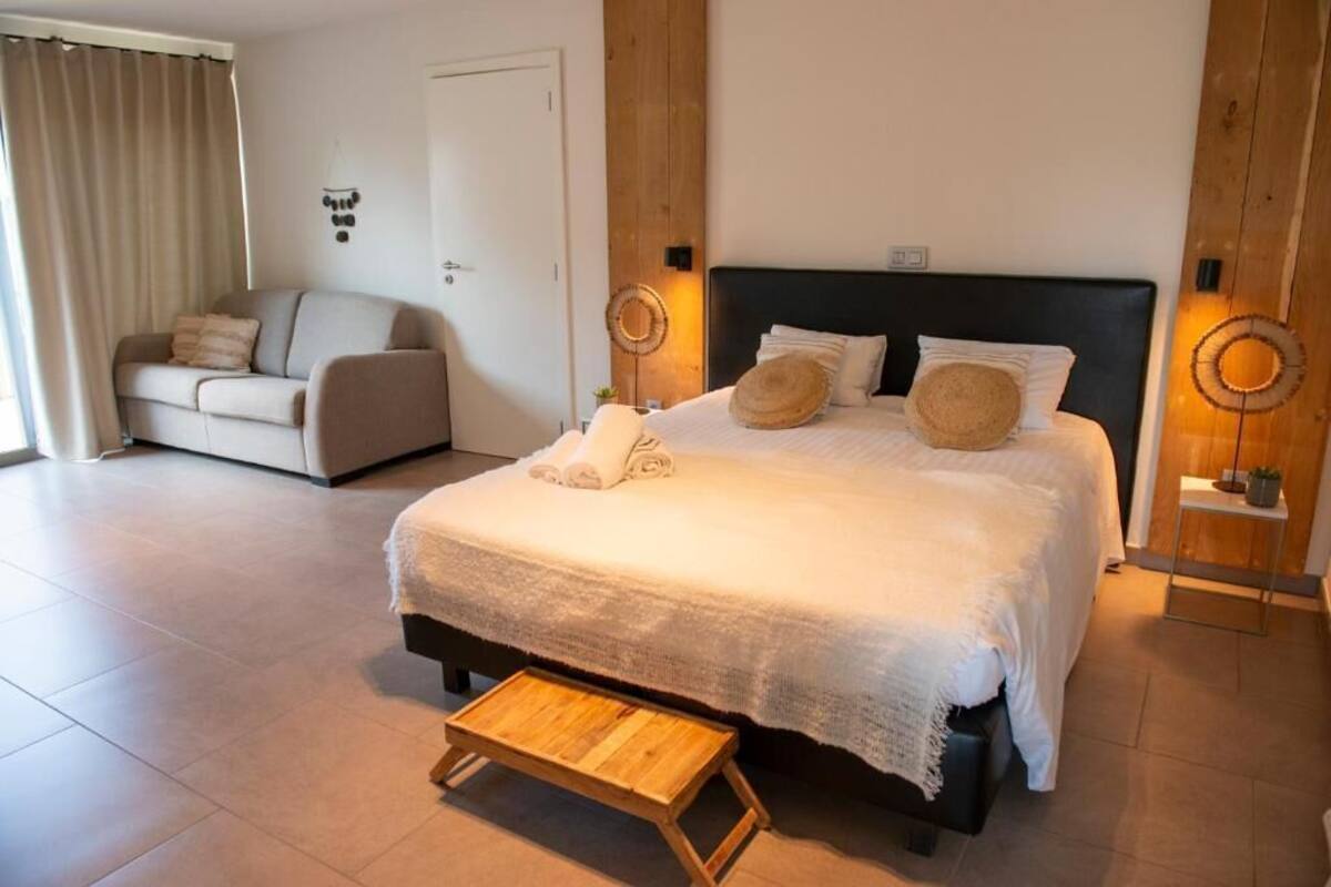 A bedroom with a bed, bedside tables, a small wooden stool, a sofa, and a door.