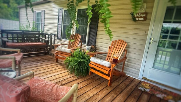 Eine Holzterrasse mit Adirondack-Stühlen, einem kleinen Tisch und einem Blumentopf.