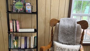 Ein Holzhocker mit Kissen, ein Bücherregal mit Büchern und einem Korb, sowie ein Fenster mit Blick.