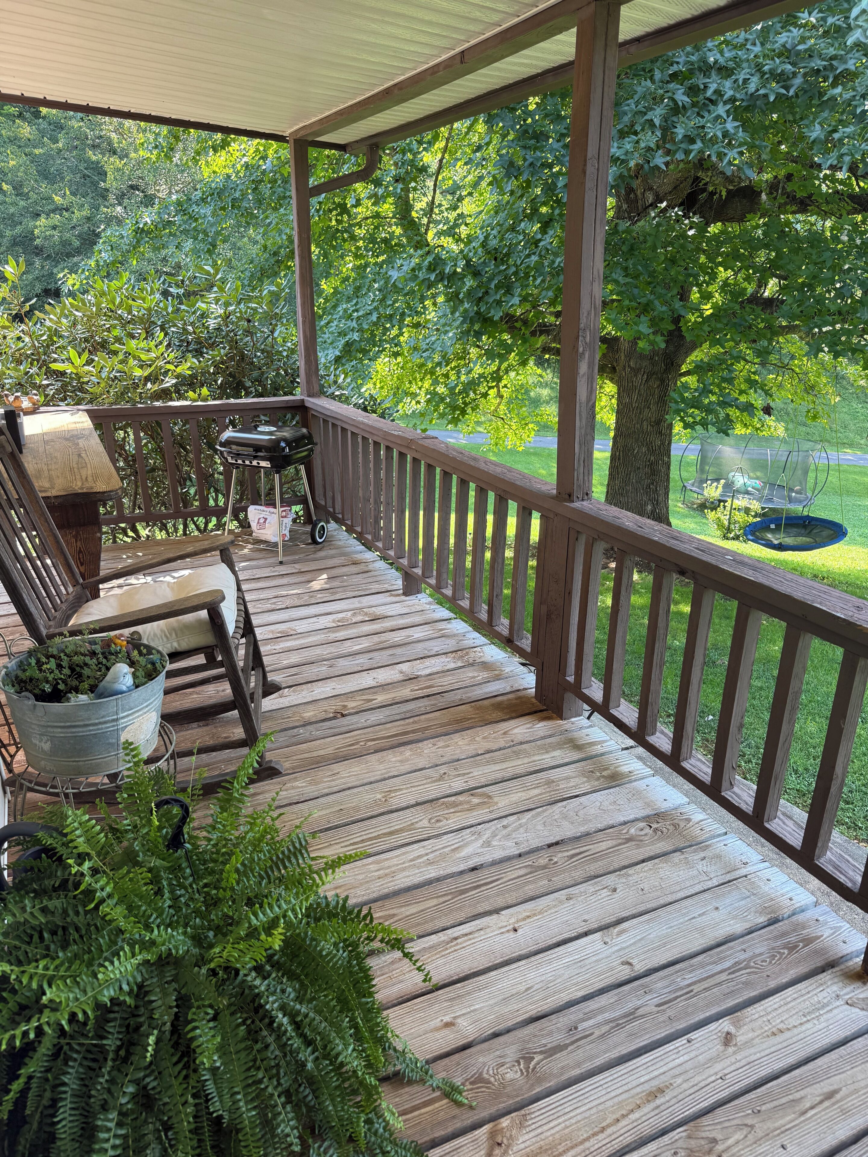A wooden deck with a grill, outdoor seating, and a hanging chair.