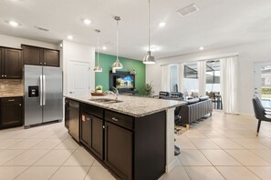 A modern kitchen with a large island, stainless steel appliances, pendant lighting, and a view to the living area. - 5 BD/ 4.5 BA/ Windsor Cay (1252 BI) (Clermont)