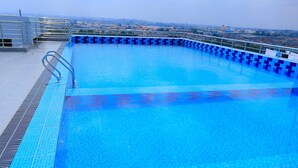 Una piscina cristallina blu con bordo piastrellato, una scala in metallo e sullo sfondo la vista dello skyline cittadino.