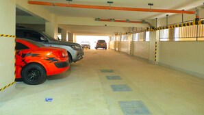 Un parcheggio sotterraneo con diverse auto parcheggiate, tubature a vista e visuale libera sull'uscita.