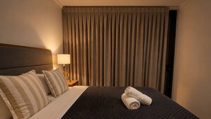 Une chambre d’hôtel avec un lit, des oreillers, une couverture, une lampe et un rideau.