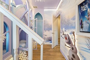 Ein Kinderzimmer mit einem Bett, einer Spielecke und einer Wandmalerei eines verschneiten Waldes.
