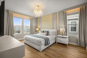 Een moderne slaapkamer met een groot bed, nachtkastjes, een kroonluchter en grote ramen.