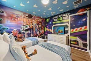 Una habitación infantil con un mural con tema espacial, televisión y juguetes.