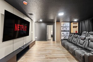 A modern living room with a large flat-screen TV, a leather sofa, and a wall-mounted shelf with decorative items. - Resort Amenities Included! 7 BD/ 6 BA/ Storey Lake 4585 TB (Kissimmee)