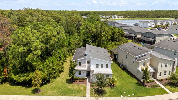 A residential area with modern houses, a grassy lawn, and a forested hill in the background. - Resort Amenities Included! 7 BD/ 6 BA/ Storey Lake 4585 TB (Kissimmee)