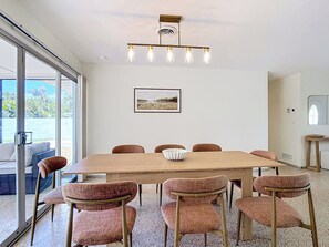 A modern dining area with a large wooden table and six upholstered chairs, a hanging light fixture, and a framed picture on the wall.