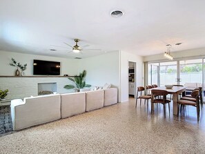 A modern living room with a sofa, dining table, chairs, and a TV.