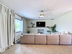 A living room with a sectional sofa, a flat-screen TV mounted above a fireplace, and a ceiling fan.