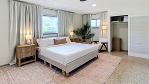 A bedroom with a bed, two bedside tables, a nightstand, a potted plant, a chair, a wardrobe, and a window with curtains. - Beach House Oasis - Steps from Ocean Access (Venice)