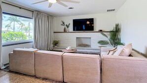 A modern living room with a sectional sofa, a flat-screen TV, a fireplace, and a ceiling fan. - Beach House Oasis - Steps from Ocean Access (Venice)