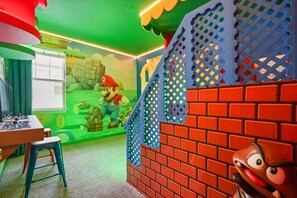 Ein Zimmer mit einem Mario-Themen-Spielbereich, darunter eine Mauer aus Ziegelsteinen, ein Fenster und ein Tisch mit Spielzeug.