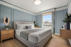 Une chambre à coucher avec un lit, des tables de chevet, une commode, une fenêtre donnant sur un beau paysage et une plante en pot.