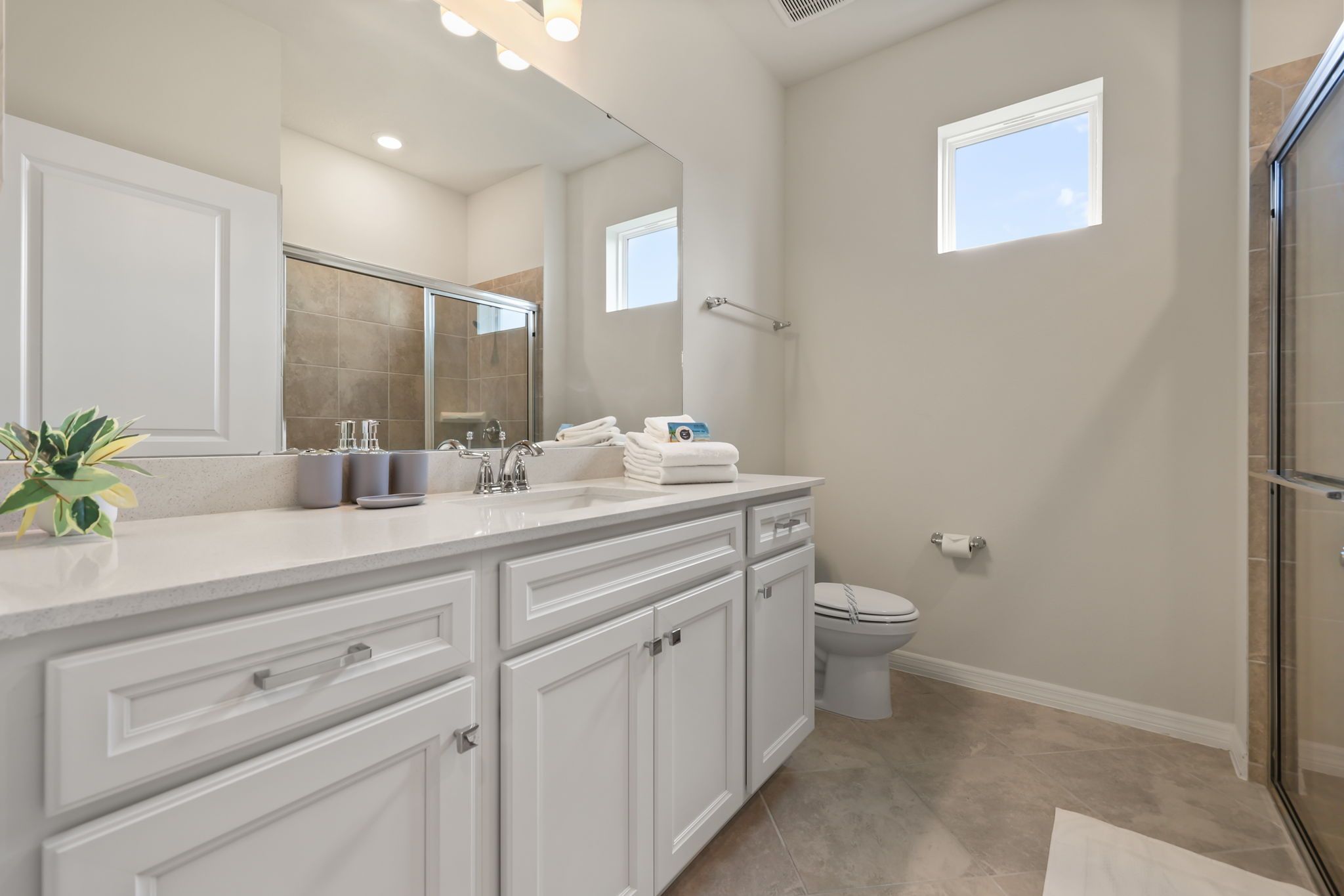 Un baño moderno con un espejo grande, muebles blancos y una cabina de ducha de vidrio.