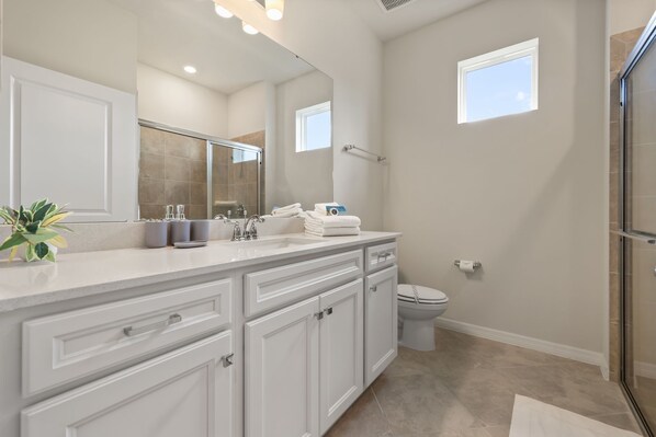 Une salle de bain moderne avec un grand miroir, des meubles blancs et une cabine de douche en verre.