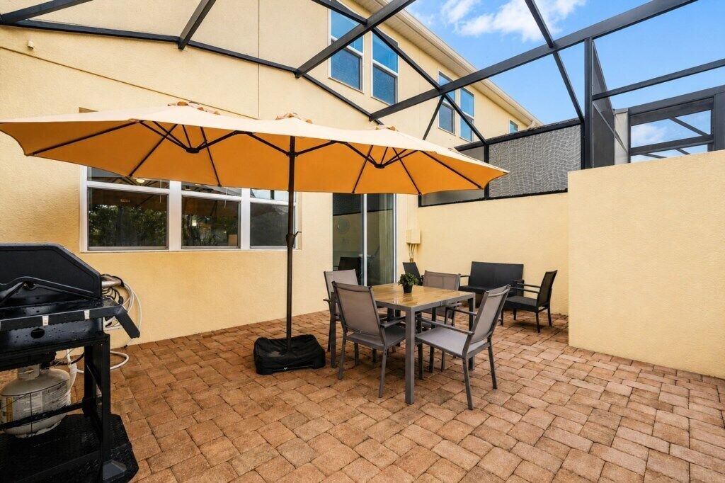 An outdoor patio with a grill, table, chairs, and an umbrella.