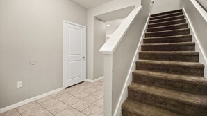 A staircase with carpeted steps leading to a landing, a white door, and a light-colored wall with a power outlet. - 4 BD/ 3.5 BA/ Compass Bay (3183 TC) (Kissimmee)