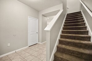 A staircase with carpeted steps leading to a landing, a white door, and a light-colored wall with a power outlet. - 4 BD/ 3.5 BA/ Compass Bay (3183 TC) (Kissimmee)