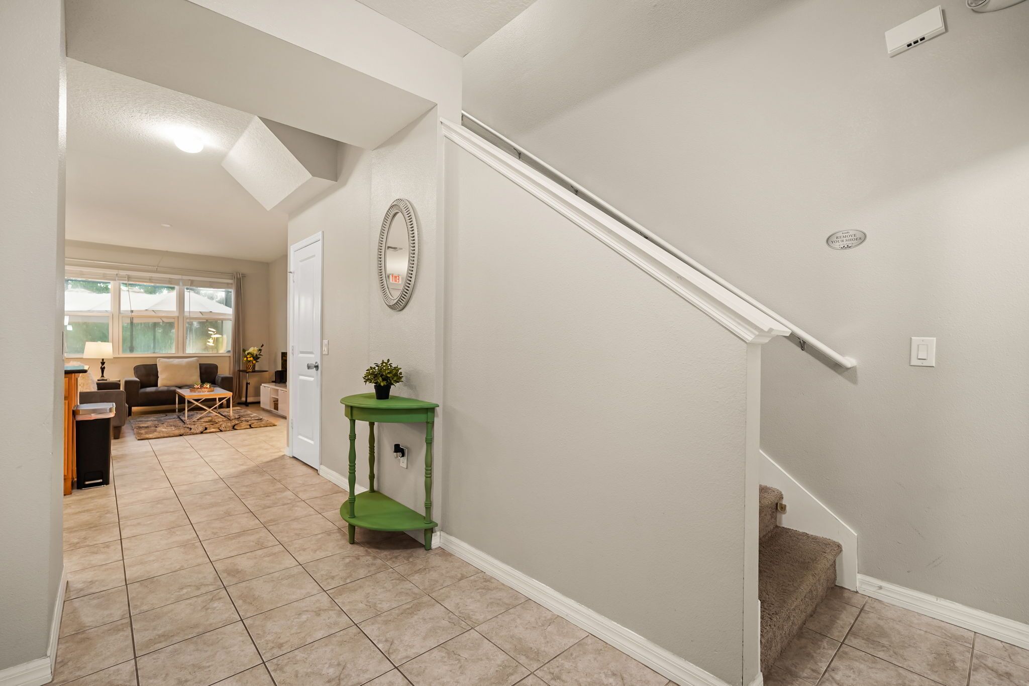 Un couloir avec un escalier, une console verte et un miroir au mur.