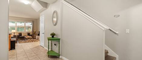 Un couloir avec un escalier, une console verte et un miroir au mur.