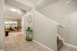 Un couloir avec un escalier, une console verte et un miroir au mur.