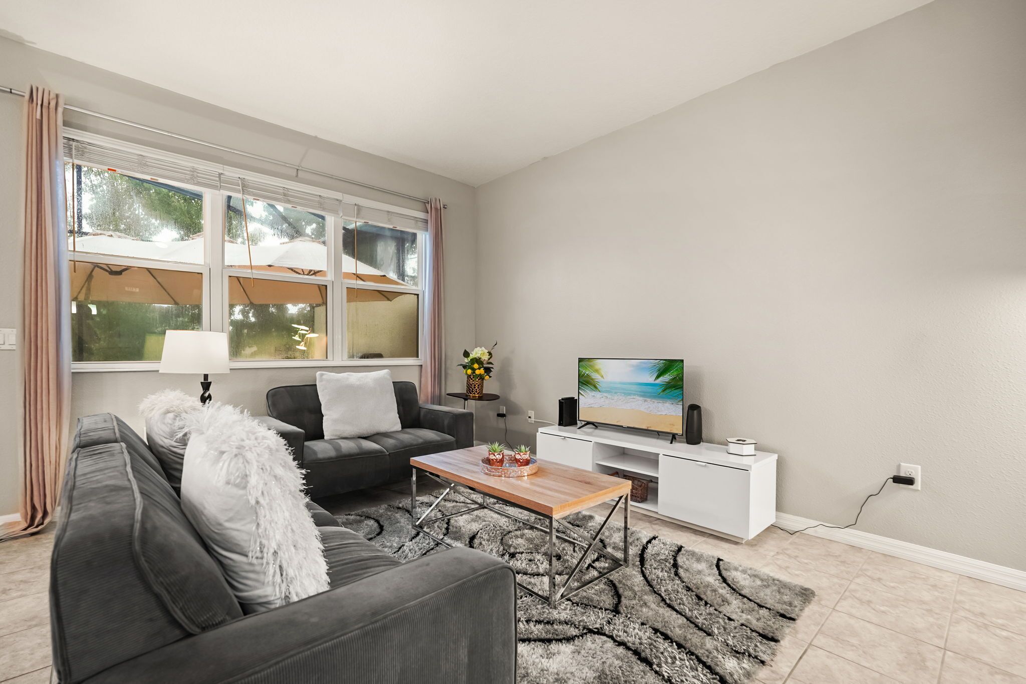 Un salon moderne avec un canapé, une table basse, un téléviseur et une vue sur l’extérieur grâce à de grandes fenêtres.