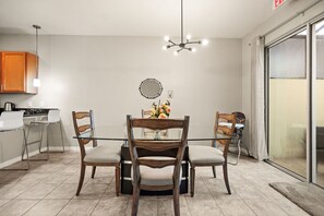 A dining area with a glass table, wooden chairs, a chandelier, and a kitchen in the background. - 4 BD/ 3.5 BA/ Compass Bay (3183 TC) (Kissimmee)