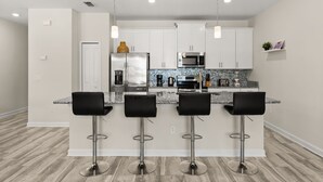 A modern kitchen with white cabinets, stainless steel appliances, a granite countertop, and three black bar stools. - 4 BD/ 3 BA/ Storey Lake (3071 GS) (Kissimmee)