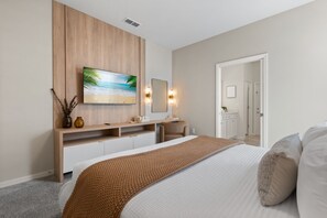 A modern bedroom with a large bed, a wooden dresser, a flat-screen TV, and a mirror. - 7 BD/ 5.5 BA/ Windsor Cay (16115 CC) (Clermont)