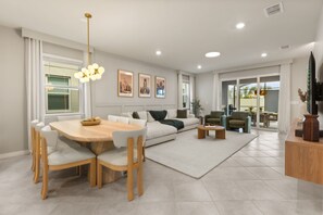 A modern living room with a dining area, a sofa set, a coffee table, and a TV on a wooden cabinet. - 7 BD/ 5.5 BA/ Windsor Cay (16115 CC) (Clermont)