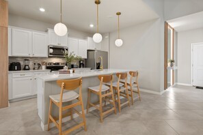 A modern kitchen with white cabinetry, stainless steel appliances, a central island with bar stools, and pendant lighting. - 7 BD / 5.5 BA / Windsor Cay 16115 CC (Clermont)