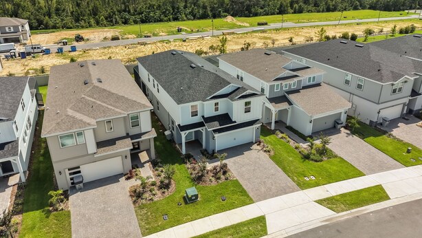 Un quartier résidentiel avec des maisons modernes à deux étages, une allée pavée et un paysage boisé en arrière-plan.