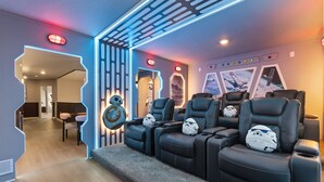 Une pièce dotée d’un coin salon avec des fauteuils en cuir noir et des coussins à l’effigie de Star Wars, d’un mur orné d’un motif lumineux géométrique et d’une affiche de Star Wars.