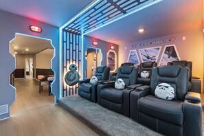 A room with a seating area featuring black leather chairs and Star Wars-themed pillows, a wall with a geometric light design, and a Star Wars poster. - 7 BD/ 5.5 BA/ Windsor Cay (16115 CC) (Clermont)