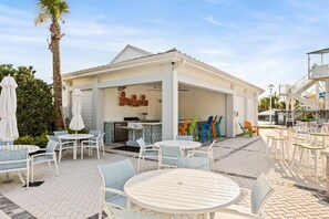 An outdoor seating area with white tables and chairs, a covered patio, and a sign that reads "RUMBRELLI". - 7 BD/ 5.5 BA/ Windsor Cay (16115 CC) (Clermont)