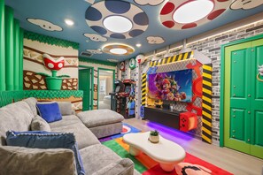 A room with a sofa, gaming console, and a wall with a Mario-themed mural. - Magical Rooms & Game Zone 5 BD/ 4.5 BA/ Windsor Cay - 16214 CC (Clermont)