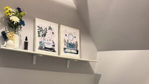 A bathroom with a toilet, a towel rack with folded towels, a trash bin, and two framed artworks on the wall. - Cozy 1 bed,  furnished apartment (Chicago)