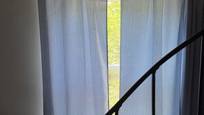A room with a window covered by a patterned curtain, a wooden chair, and a black metal staircase railing. - Cozy 1 bed,  furnished apartment (Chicago)