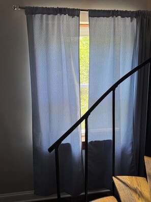 A room with a window covered by a patterned curtain, a wooden chair, and a black metal staircase railing. - Cozy 1 bed,  furnished apartment (Chicago)