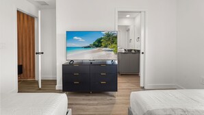 Ein Hotelzimmer mit Bett, Fernseher auf einem Nachttisch, einer Holztür und Blick auf einen Strand.