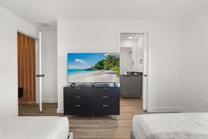 A hotel room with a bed, a TV on a dresser, a wooden door, and a view of a beach. - 3 BD/ 3 BA/ The Hub at Westside Reserve (3263 SW) (Kissimmee)