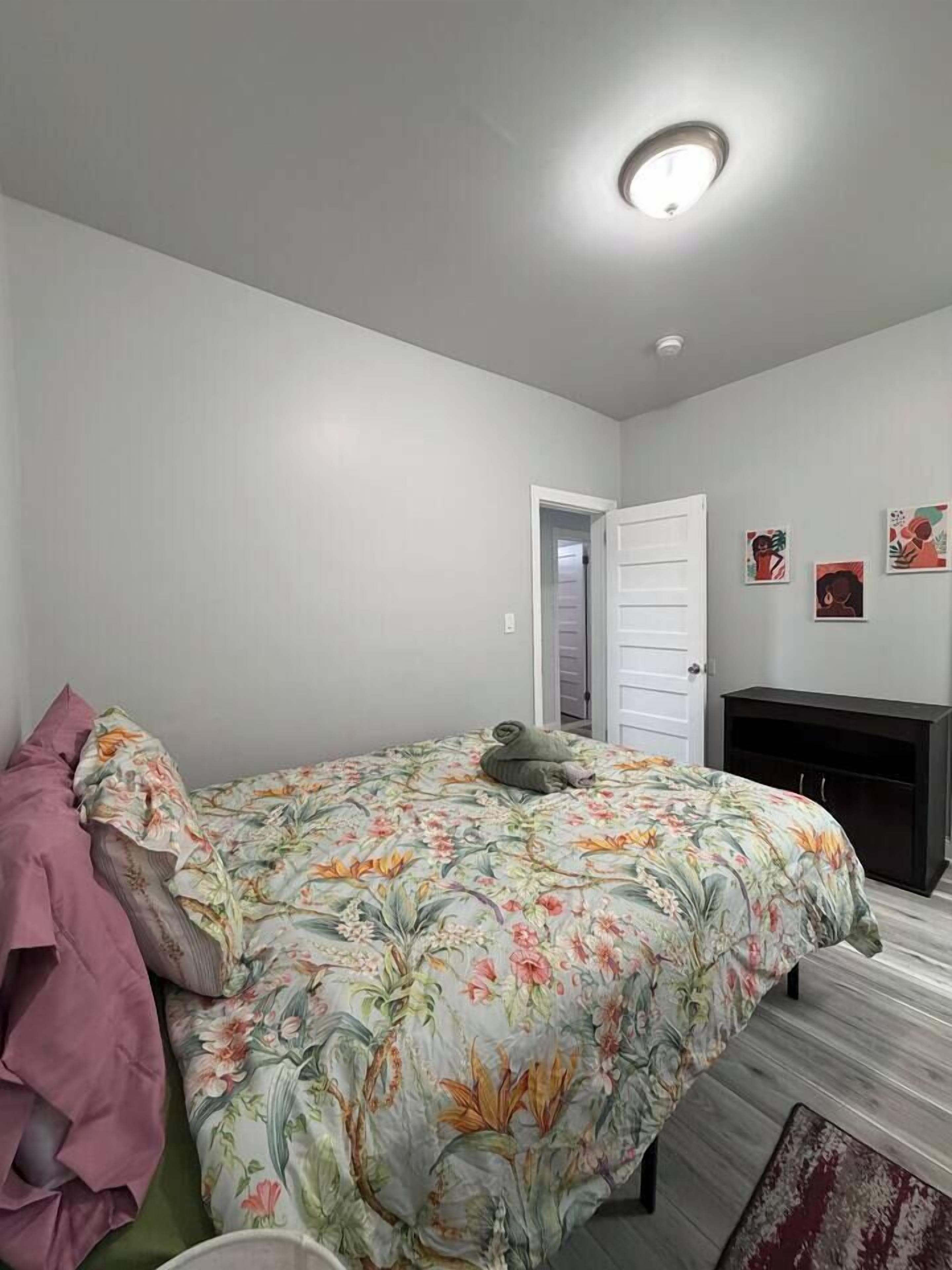 Une chambre à coucher avec un lit, une porte, une petite armoire et un mur décoré d’œuvres d’art.