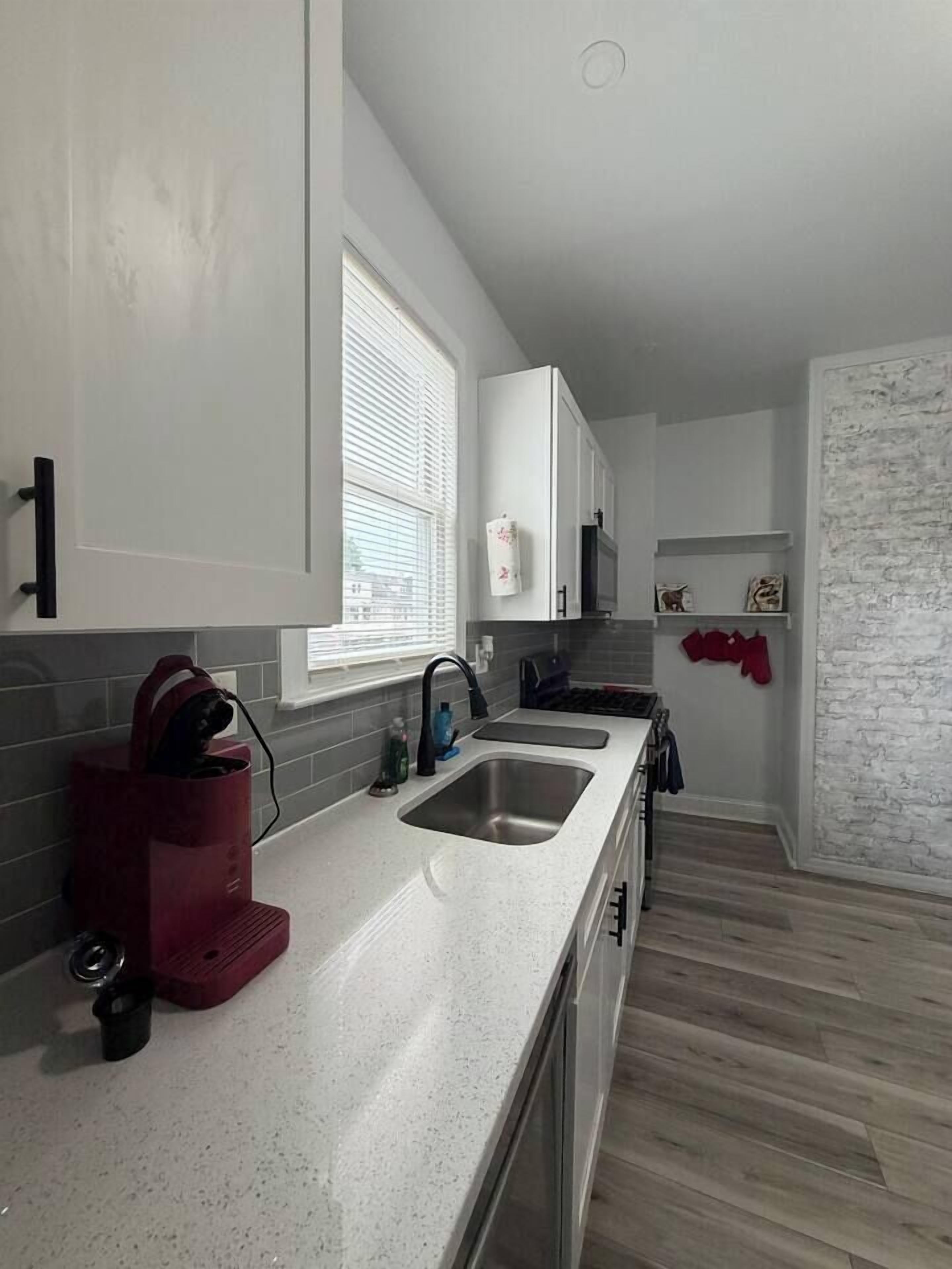 A modern kitchen with a white countertop, stainless steel sink, and a red appliance.