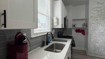 A modern kitchen with a white countertop, stainless steel sink, and a red appliance.