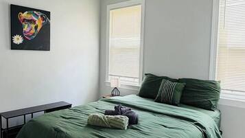 A bedroom with a bed, a desk, and a painting on the wall.