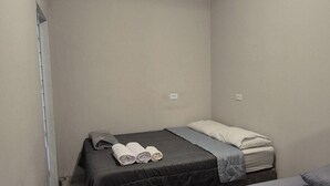A small, single-room accommodation with two beds, a ceiling light, and an air conditioning unit.